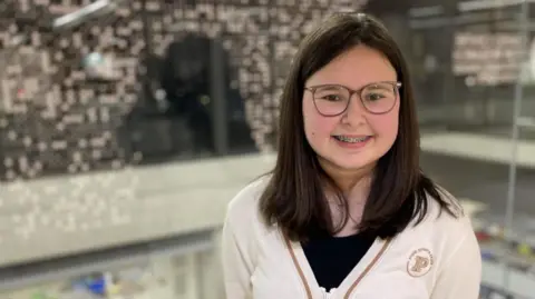 BBC Una adolescente de cabello oscuro sonríe a la cámara, vestida con una rebeca blanca.
