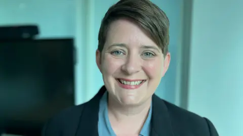La ministra de Igualdad, Olivia Bailey, sonriendo ante la cámara.