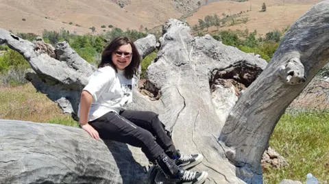 Una adolescente sentada en un árbol caído con corteza blanqueada por el sol.