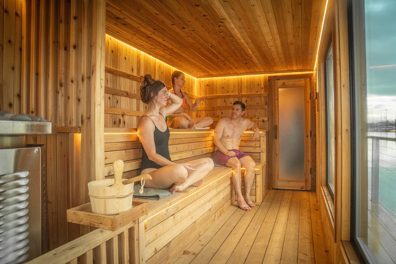 Dos mujeres y un hombre sentados dentro de una sauna