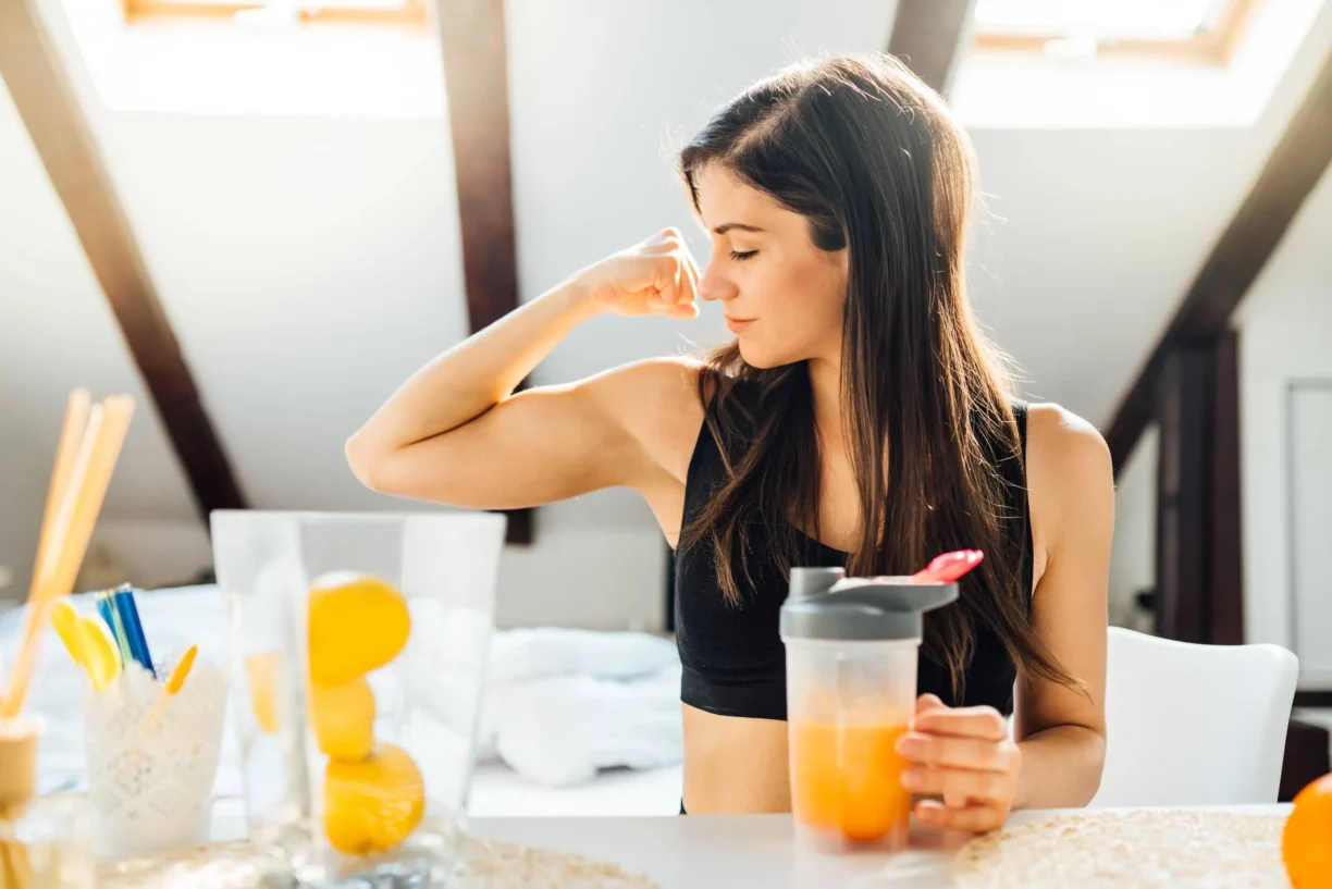 Mujer en casa bebiendo polvo de aminoácidos vitamínicos con sabor a naranja