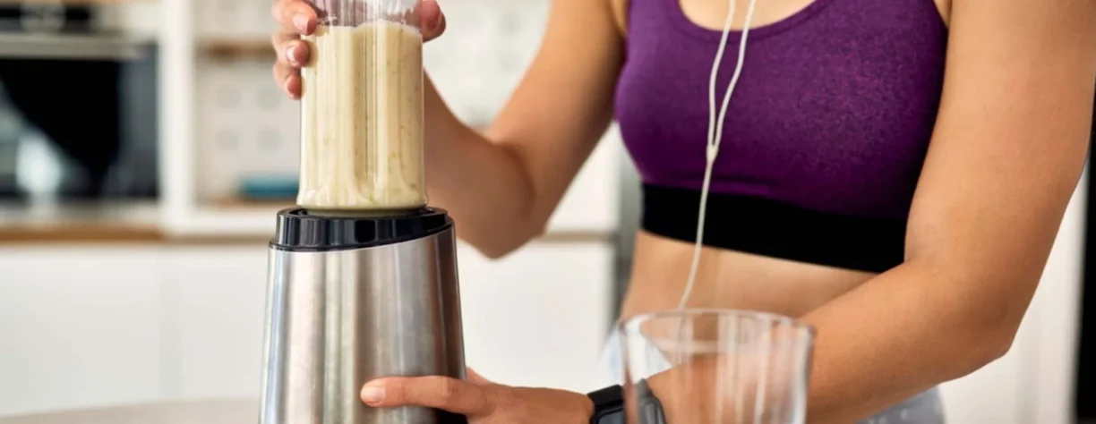 Mujer deportiva usando licuadora y preparando batidos en la cocina.