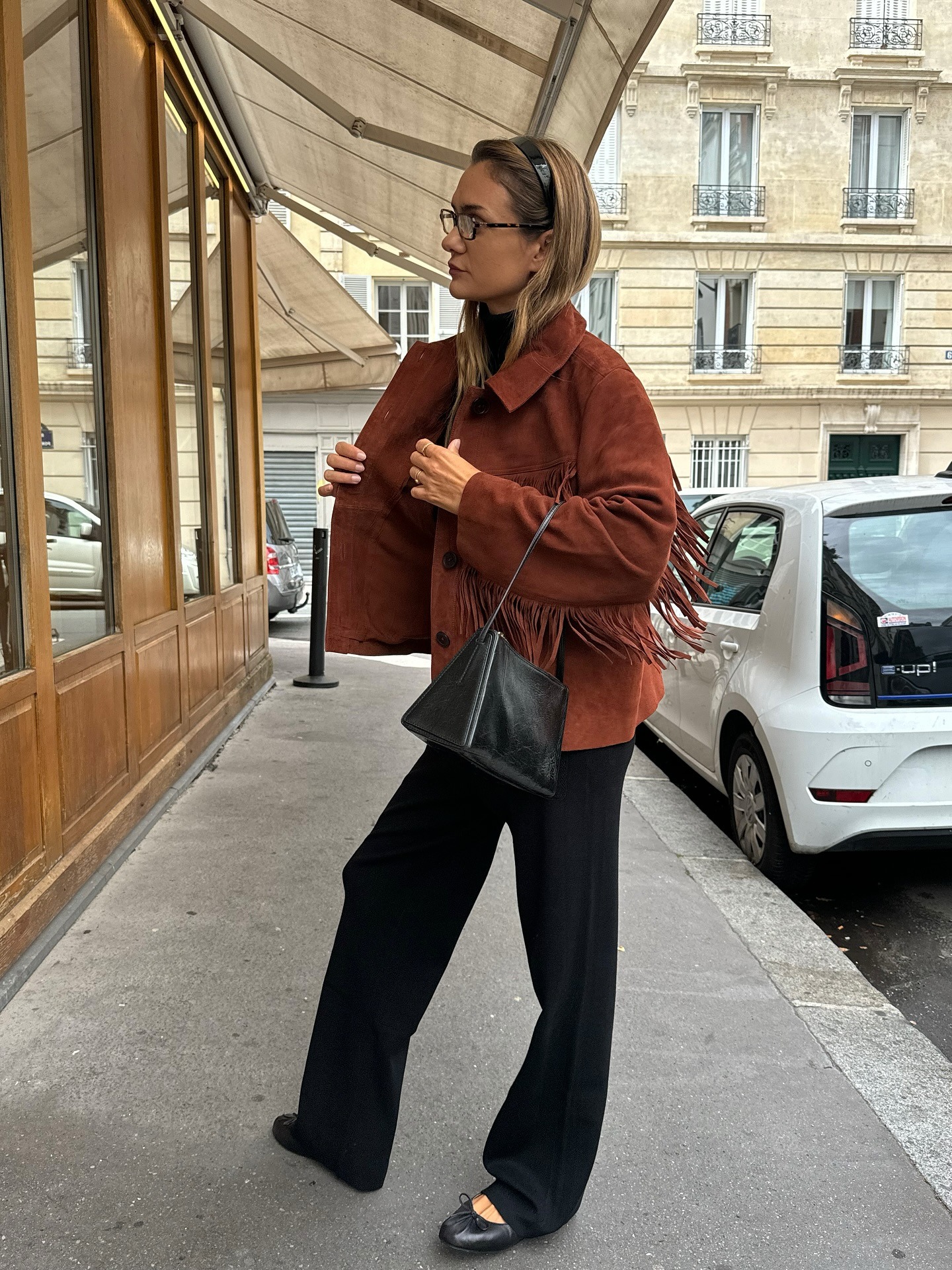 Anne lleva una chaqueta con flecos, pantalones anchos negros y bailarinas negras.