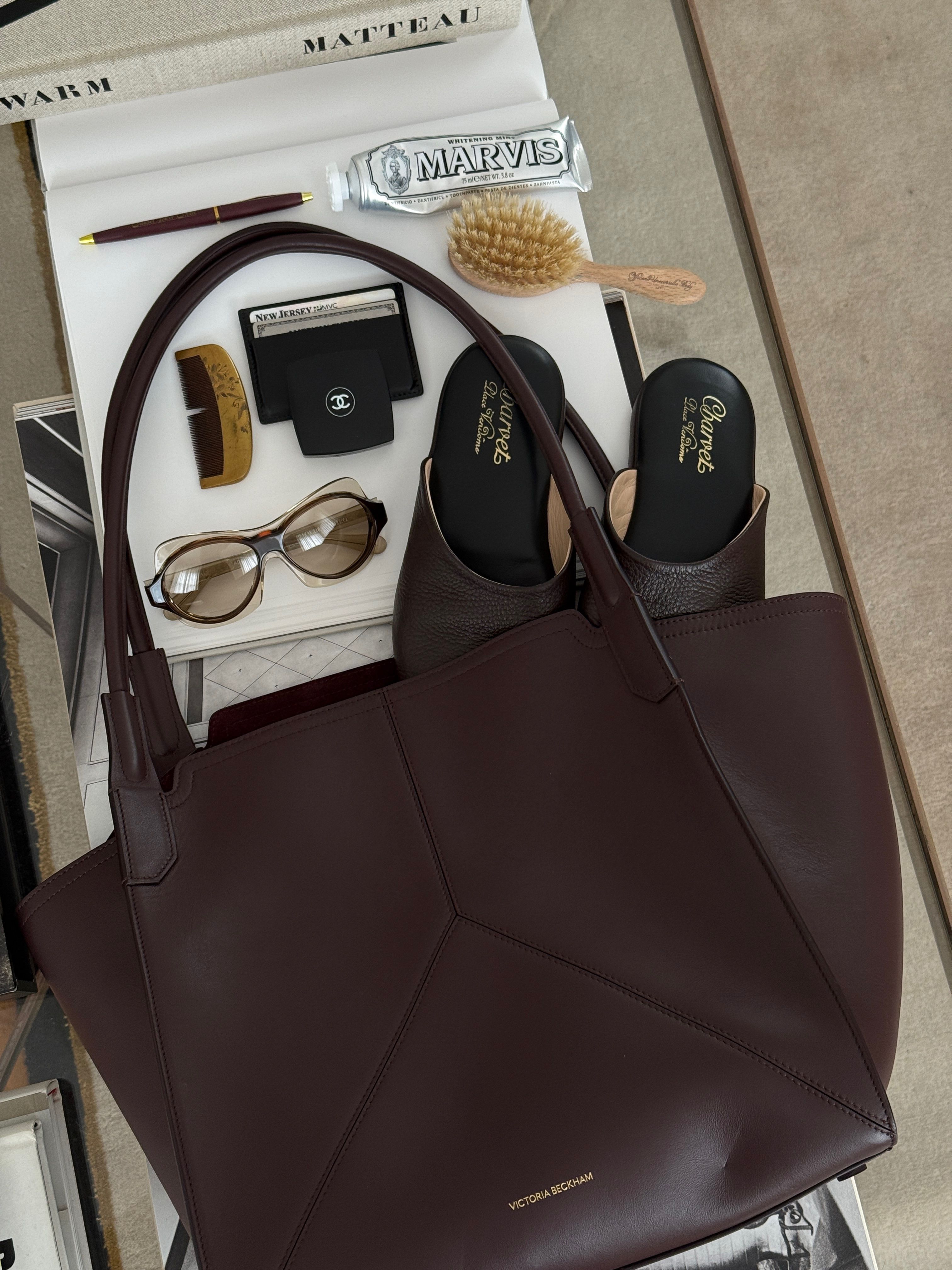 una bolsa sobre una mesa junto a un cepillo, un par de zapatos, un peine y gafas de sol