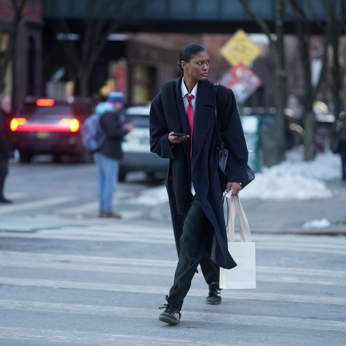 Nueva York, Nueva York 13 de febrero: se ve a una persona con un abrigo de lana azul marino, una camisa de cuello blanco, una corbata con estampados rojos, una bufanda de punto negro, un pantalón negro y unas zapatillas de adidas negras, mientras lleva una bolsa de hombro de cuero negro y una bolsa de compras de papel 2026 en la ciudad de Nueva York en 2026. (foto de 305pics/getty images)