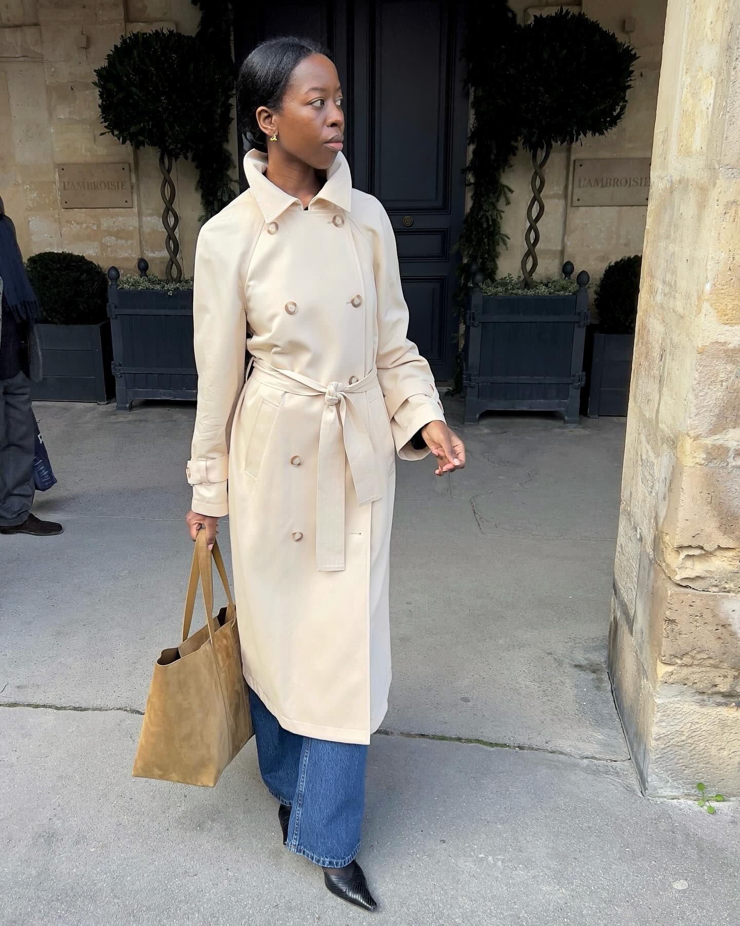 Sylvie lleva una gabardina, vaqueros, bombas y una bolsa tote de gamuza.