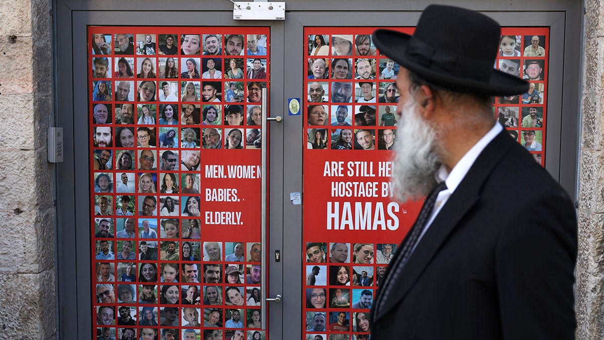 Un israelí pasa por delante de una pancarta con los retratos de israelíes presos como rehenes