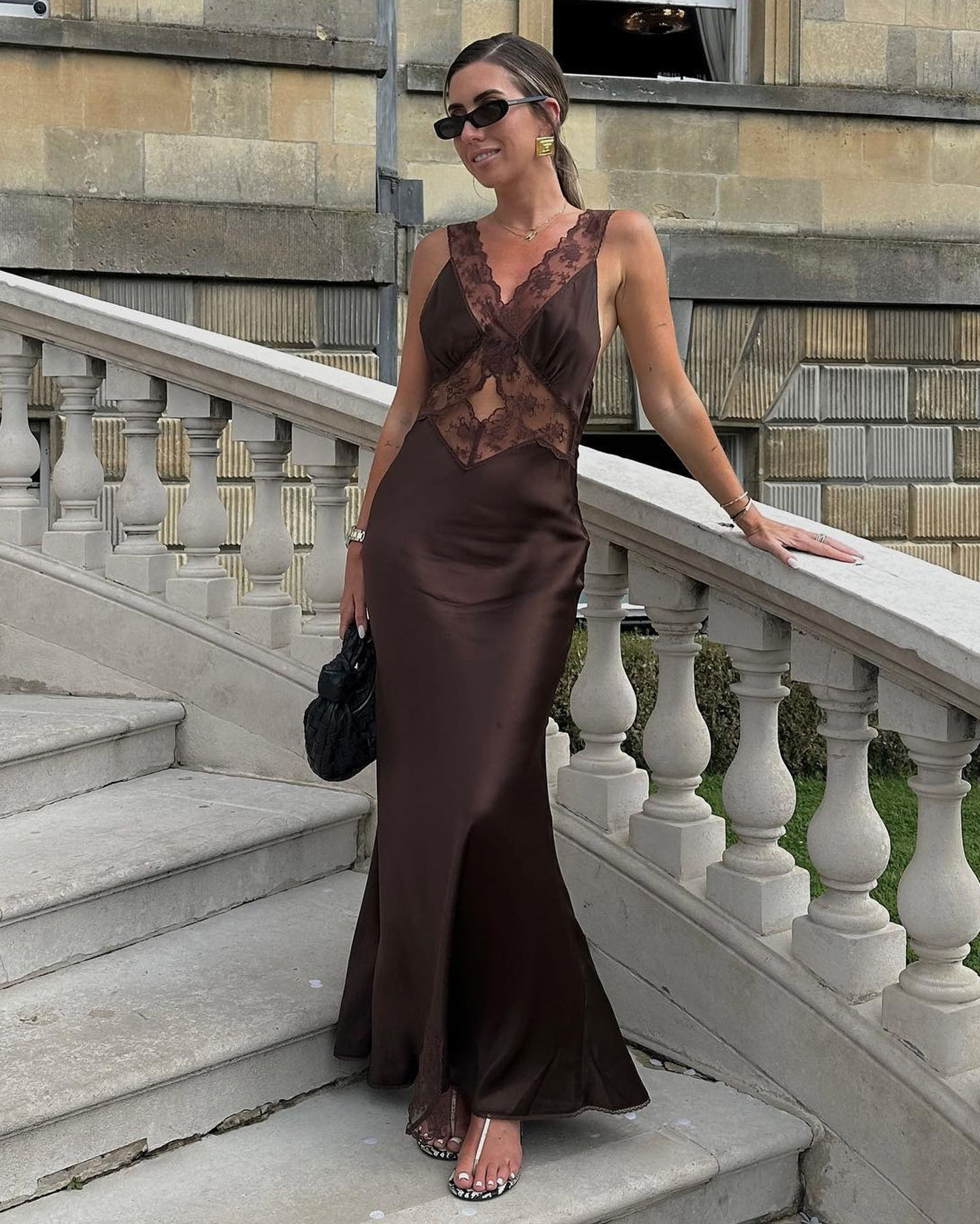 La influencer de estilo británico Hannah Lewis pone en una boda con gafas de sol rectangulares, una falda maxi de satén negro con puntas y sandalias de piel de serpiente.